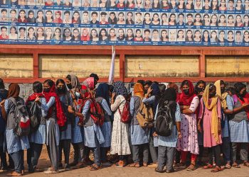School children await bus transport beneath a billboard with photographs of successful students outside a school in Nooranad, Kerala, India, Friday, March 4, 2022. Slowly but steadily, life in South Asia is returning to normal, and people hope the worst of the COVID-19 pandemic is behind them. (AP Photo/R S Iyer)